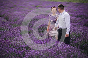 Young couple in love hugging and walking in a lavender field on summer cloudy day. girl in a luxurious purple dress and with