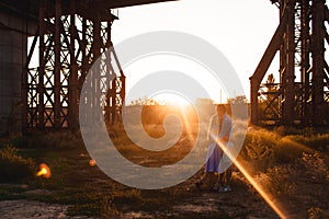 Young couple in love hugs on sunset amidst a bridge under construction. Man hugs woman closely. Outdoor portrait of couple