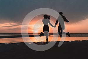 Young couple in love jumping at sunset on the beach in autumn