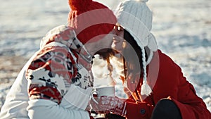 Young couple in love kiss in first snowy winter day and drink coffee. Man and woman on date meeting christmas. Happy