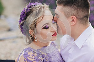 Young couple in love kissing in a lavender field on summer clody day. girl in a luxurious purple dress and with hairstyle
