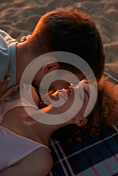 Young couple in love kissing while spending time together on the beach at sunset
