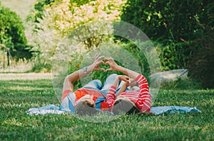 Young couple in love lies on a plaid in the park, make hands a symbol of love - the heart. Picnic for couples in love