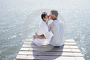 Young couple in love in light casual clothes is sitting on wooden bridge