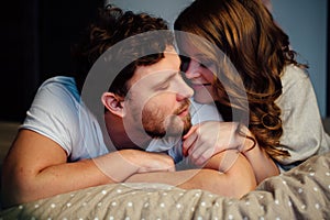 Young couple in love lying in bed in hotel, embracing on white sheets, close up