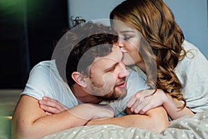 Young couple in love lying in bed in hotel, embracing on white sheets, close up