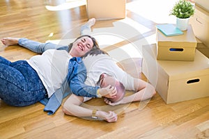 Young couple in love lying on the floor of new house arround cardboard boxes, smiling very happy for moving to a new apartment