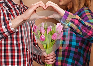 Young couple in love make a heart and hands are holding tulips.