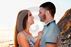 A young couple in love, a man and a woman, look at each other. Portraits. In the background, the sea and sunset. The concept of
