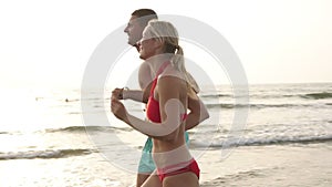 Young couple in love, man and woman run along the beach and sea waves