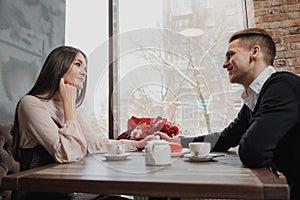 Young couple in love, man and woman, sit at a table in a cafe. St. Valentine`s Day.