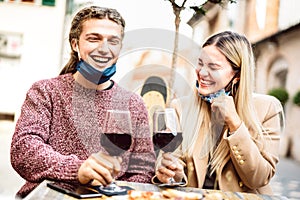 Young couple in love with open face masks having fun at wine bar outdoors - Happy millenial lovers enjoying lunch together at