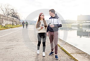 Young couple in love outdoor. Travelers with cups of coffee are walking in spring park. Beautiful sunny day. A young couple