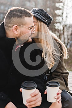 Young couple in love outdoor. Travelers with cups of coffee are walking in spring park. Beautiful sunny day. A young couple