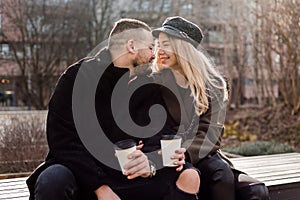 Young couple in love outdoor. Travelers with cups of coffee are walking in spring park. Beautiful sunny day. A young couple