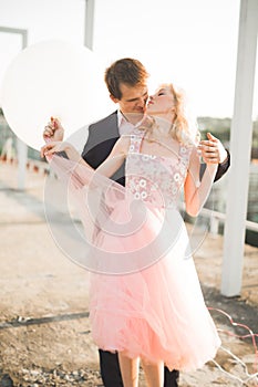 Young couple in love posing on roof with perfect city view holding hands and hugging . Beautiful sunset