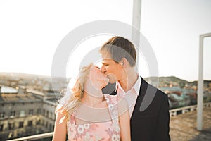 Young couple in love posing on roof with perfect city view holding hands and hugging . Beautiful sunset