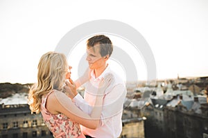 Young couple in love posing on roof with perfect city view holding hands and hugging . Beautiful sunset