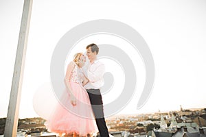 Young couple in love posing on roof with perfect city view holding hands and hugging . Beautiful sunset