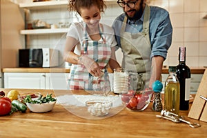 Young couple in love preparing the dough for making pizza with vegetables at home. Man and woman wearing apron, cooking