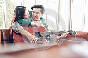 Young Couple Love Relaxing on Sofa in Living Room While Playing Guitar and Enjoyed Sing a Song at Home Together. Romantic Asian