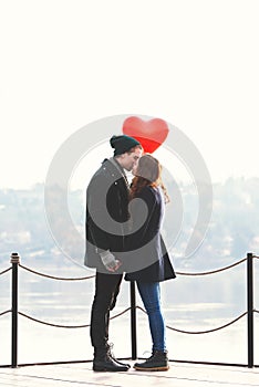 Young couple in love, at the riverside, with a red balloon