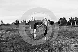 Young Couple in Love Running in a Big Open Outdoor Field in the Spring Holding Hands and Laughing