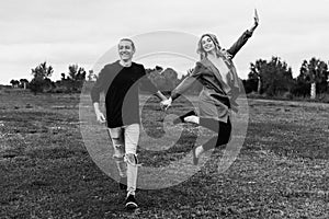 Young Couple in Love Running in a Big Open Outdoor Field in the Spring Holding Hands and Laughing