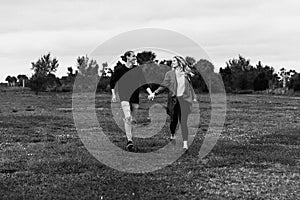 Young Couple in Love Running in a Big Open Outdoor Field in the Spring Holding Hands and Laughing