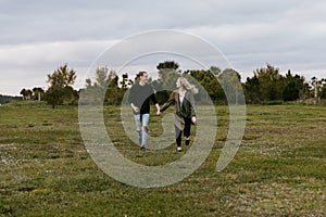 Young Couple in Love Running in a Big Open Outdoor Field in the Spring Holding Hands and Laughing