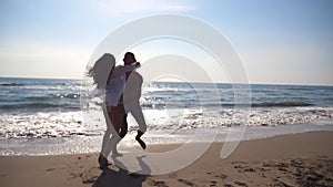 Young couple in love running on sea beach, man hug his woman and spinning around. Girl jumps into her boyfriend hands