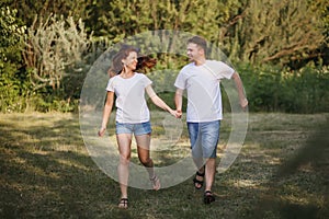 A young couple in love runs along the lawn and holds each other`s hands, smiling and having fun