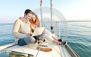 Young couple in love on sail boat having fun remote working at laptop- Happy luxury lifestyle on yacht sailboat