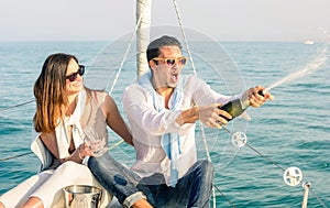 Young couple in love on sailing boat cheering with champagne wine bottle - Happy girlfriend birthday party cruise travel