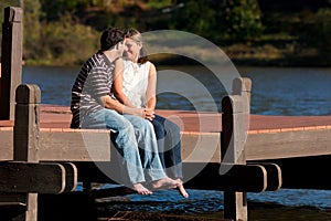 Young Couple In Love Sit Barefoot On Dock