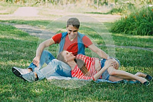 Young couple in love is sitting on a blanket in the park, the girl is lying on the guy`s lap and talking. Picnic for couples in