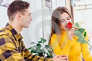 Young couple in love sitting in cafe celebrating their honymoon, man brought a red rose for his beautiful young woman,.