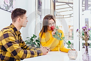 Young couple in love sitting in cafe celebrating their honymoon, man brought a red rose for his beautiful young woman,.