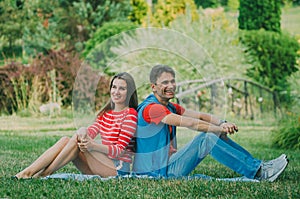 Young couple in love is sitting on the plaid in the park, back to back and enjoying the nature. Picnic for couples in love
