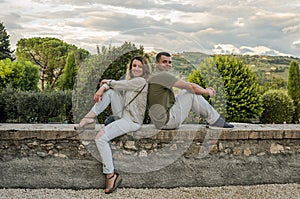 Young couple in love sitting on a stone fence overlooking the Italian mountains