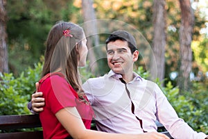 Young couple in love sitting together on a bench, the man looking at the woman, smiling