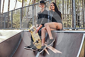 Couple in love sitting together on a ramp in the skate park at the summertime