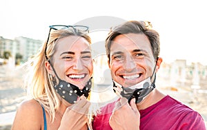 Young couple in love smiling with open face mask - New normal life style and relationship concept with happy lovers