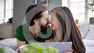 Young couple in love with tablet on bed indoors at home, cuddling.