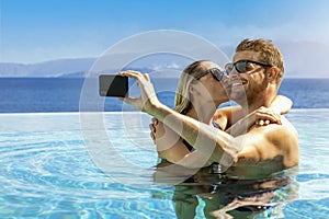 Young couple in love taking selfie in infinity swimming pool. romantic getaway, summer vacation