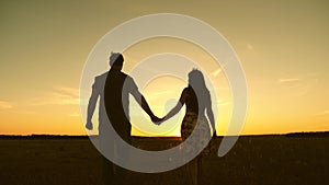 Young couple in love walking across the field holding hands. girl and man go to the sunset. happy family walks in the