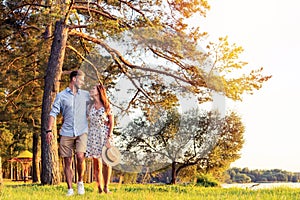 Young couple in love walking in the autumn park holding hands looking in the sunset.