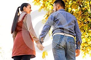 Young couple in love walking in the autumn park holding hands looking in the sunset