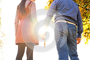 Young couple in love walking in the autumn park holding hands looking in the sunset