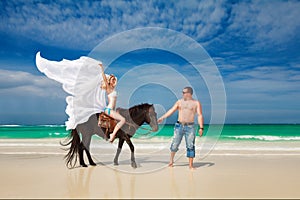 Young couple in love walking with the horse on a tropical beach.